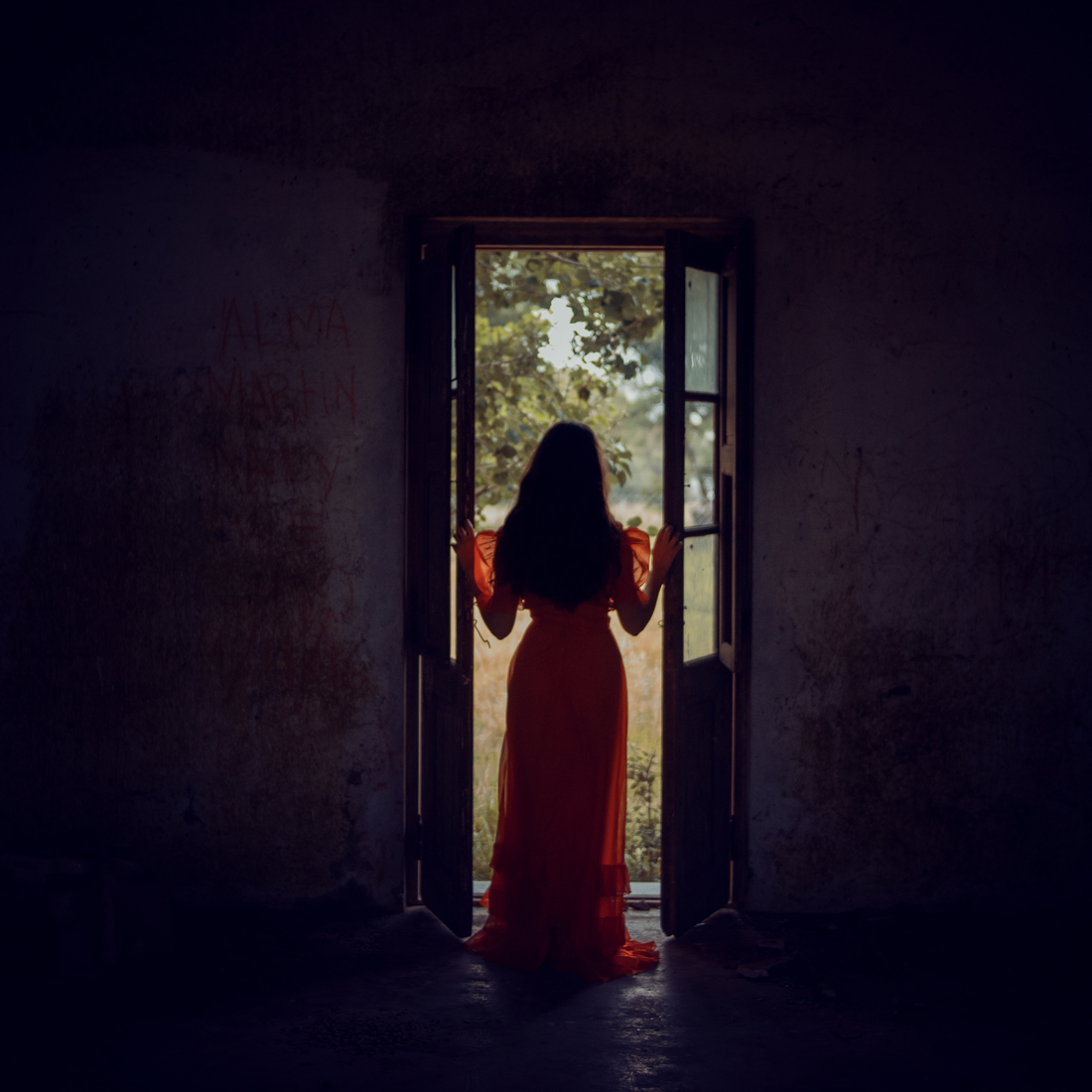 Woman standing in the doorway of a room looking outside.  She is emerging from the shadows