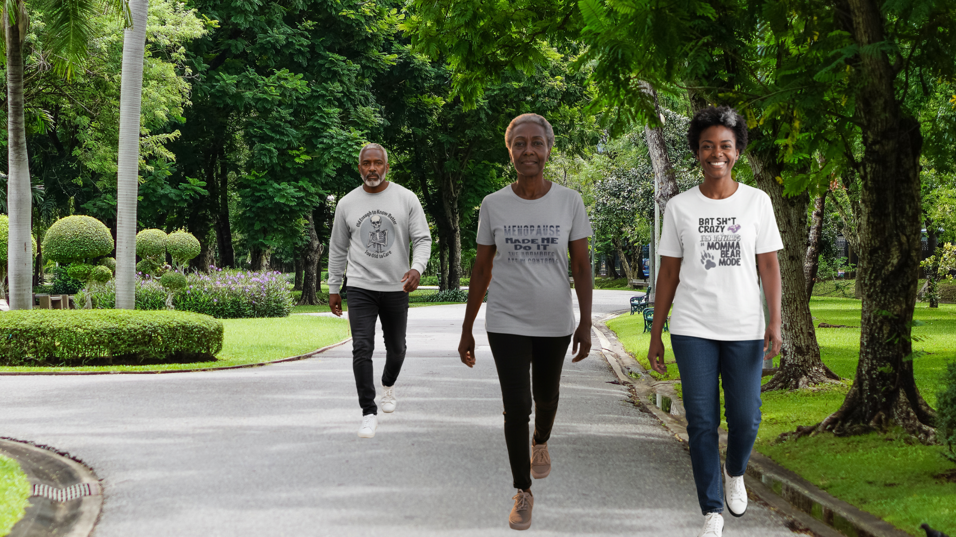 Three people walking on a path in a park wearing t-shirts with text.